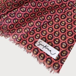 Gros plan sur un foulard en tissu rouge avec de petits motifs circulaires et une étiquette blanche indiquant Sakura cousue sur le bord effiloché.