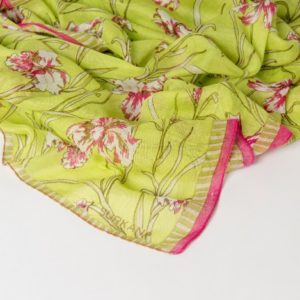 Un tissu vert clair à motif floral rose et blanc, avec une bordure rayée rose et or, est drapé sur une surface blanche.