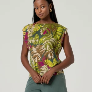 Femme aux longs cheveux bruns portant un top sans manches avec drapé Vert et un pantalon vert, debout devant un fond uni et clair.